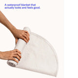 Person rolling up the Dame Thro Waterproof Sex Blanket Oat showcasing its waterproof feature.