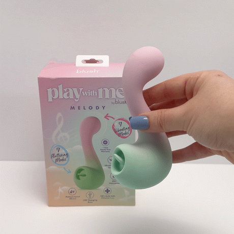 Hand holding Play With Me Massager Melody Pink toy beside the product packaging featuring playful design.