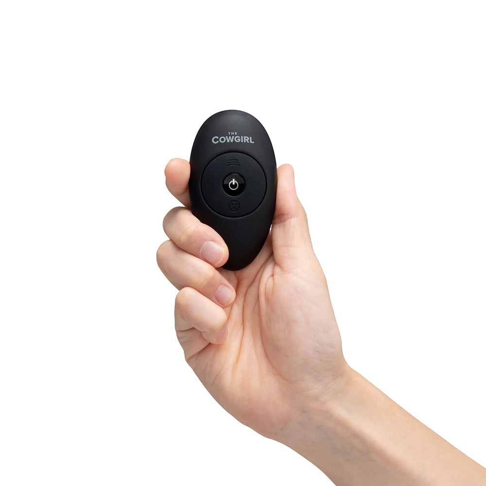 A hand holding the remote control for The Cowgirl Saddle Machine Black, designed for easy operation.