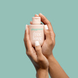 Hands holding Playground Free Love Water-Based Personal Lubricant 3.7 Oz against a mint green background.