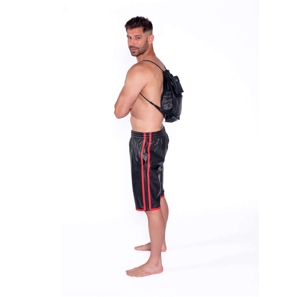 Man wearing a black and red outfit with a leather backpack, posed sideways for a fashion shoot.