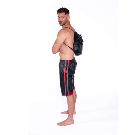 Man wearing a black and red outfit with a leather backpack, posed sideways for a fashion shoot.