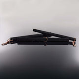 Coquette Pleasure Spreader Bar Black with velvet finish and metal accents placed on a reflective surface.