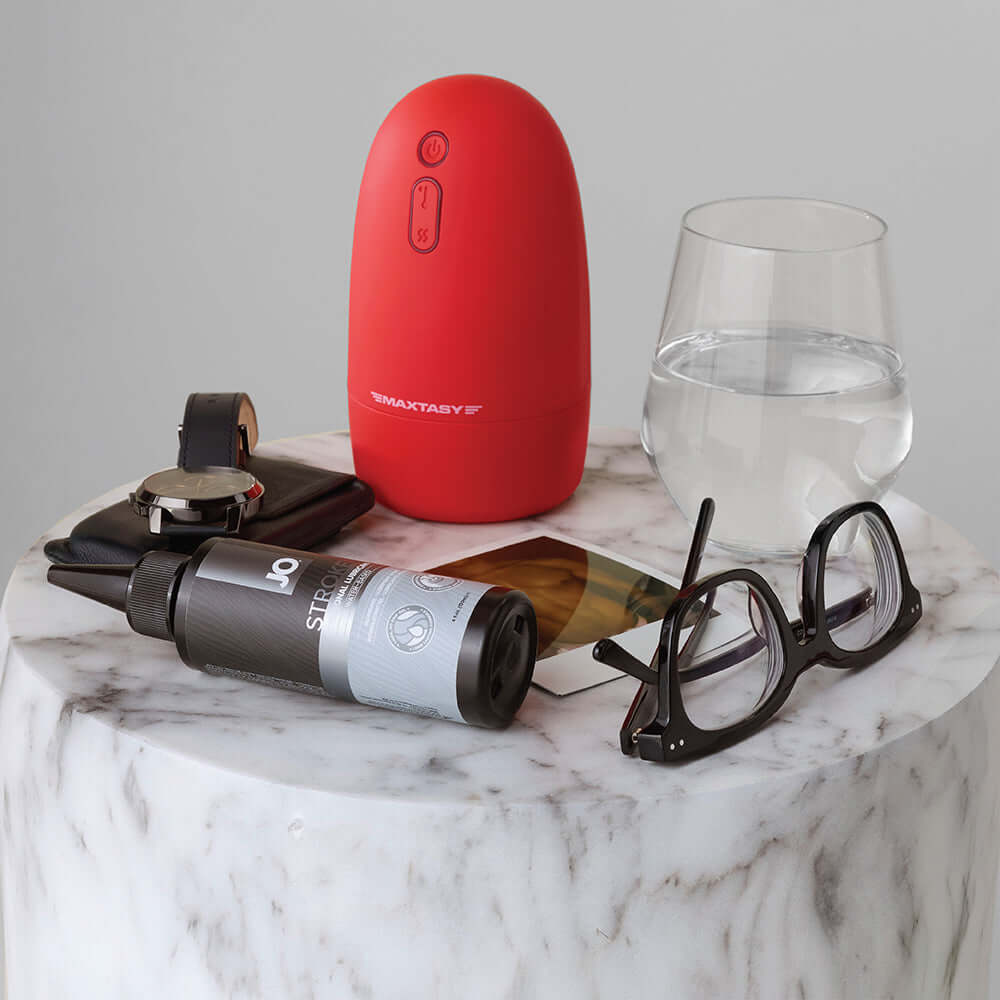 JO Stroker Lubricant 4 Oz alongside a red sex toy and personal items on a marble table.