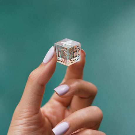 A hand holding a clear decorative cube with intricate patterns, showcasing elegance against a blurred background.