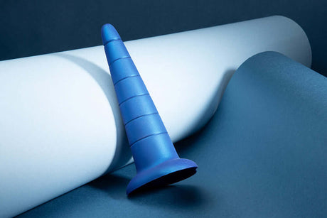 b-Vibe Anal Stretcher Training Cone on a blue surface with white paper, designed for anal training and gradual expansion.