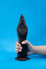 b-Vibe Vibrating Silicone Fisting Dildo held by a hand against a solid blue background.
