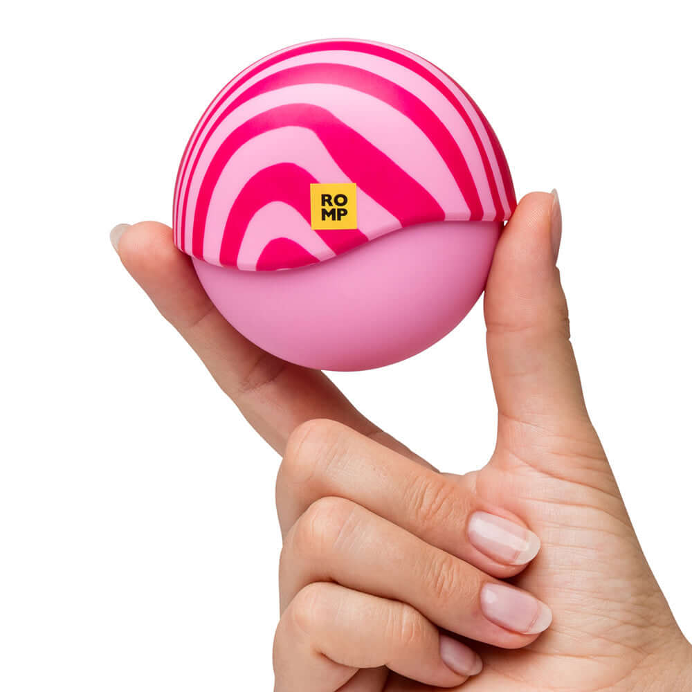 ROMP Spin Travel Rechargeable Clitoral Stimulator held in a hand, featuring a pink and white striped design.