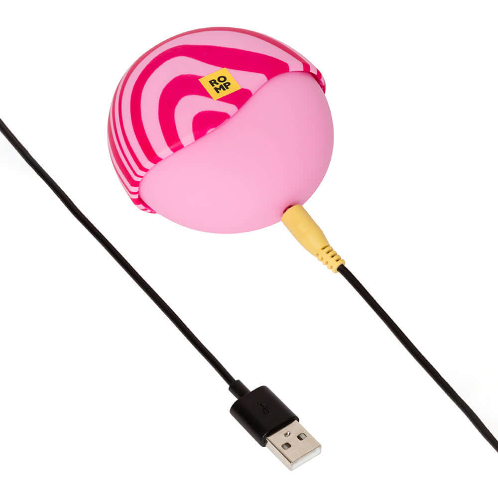 ROMP Spin Travel Rechargeable Clitoral Stimulator in pink with USB charging cable.
