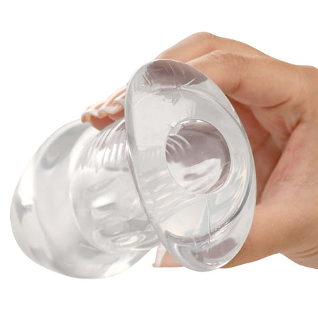 Close-up of the Master Series Dicked Clear Hollow Anal Plug Large held in hand, showcasing its transparent design.