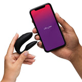 We-Vibe Chorus Couples Vibrator with Remote Control Black held with smartphone displaying app interface.