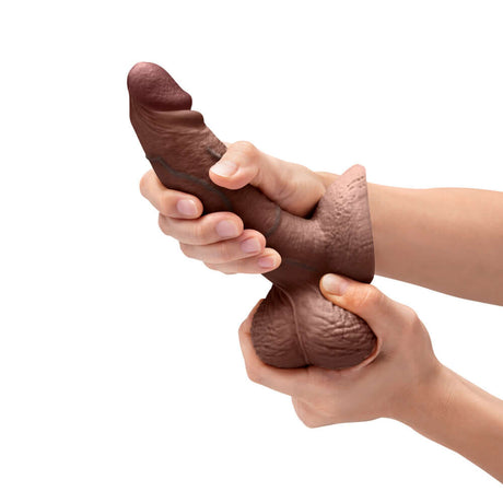 b-Vibe Slipskin Realistic Silicone Dildo 6 inch Girthy Brown being held and squeezed, showcasing its realistic design.