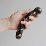 Hand holding the Chakrubs Anahata Curve Rhodonite Wand, a crystal pleasure tool for heart opening and emotional balance.