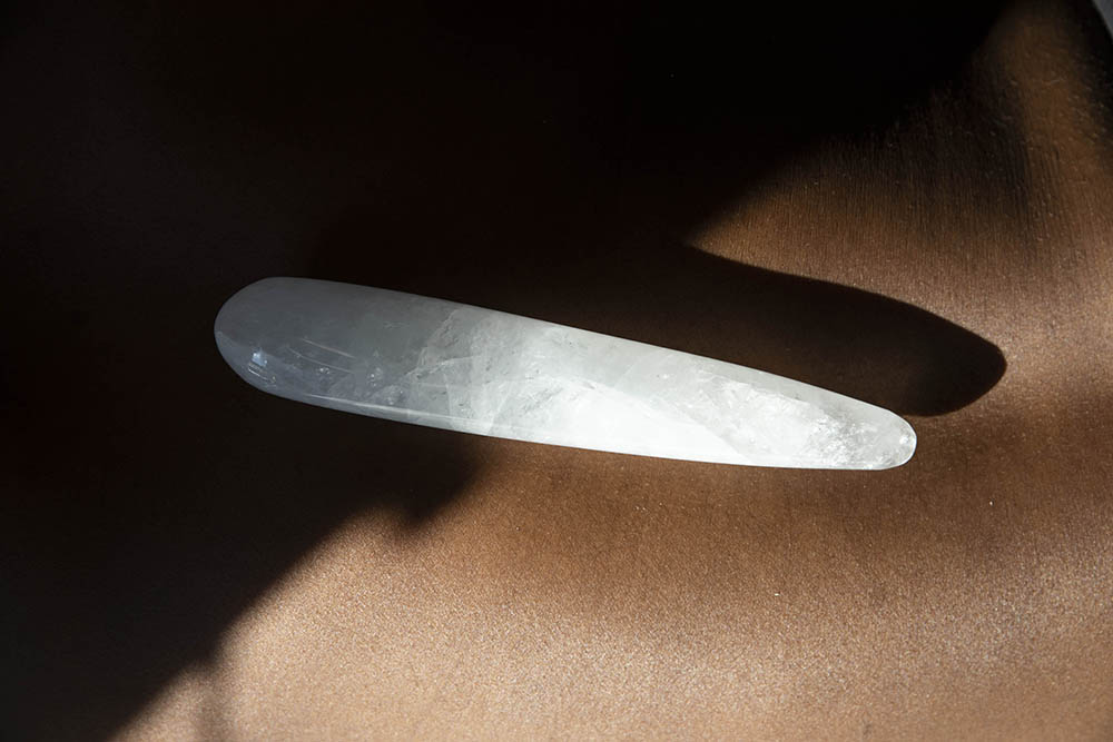 Chakrubs Prism Original Clear Quartz Wand resting on a brown surface, highlighting its smooth, translucent design.