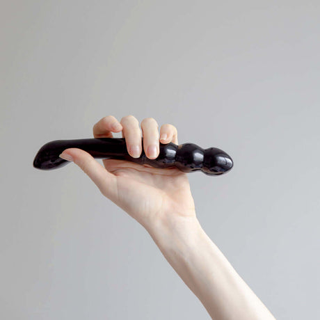 Hand holding the Chakrubs Xaga Viper Obsidian Wand against a neutral background, showcasing its unique curvature.