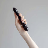 A hand holding the Chakrubs Xaga Viper Obsidian Wand, showcasing its unique curvature and ridged design.