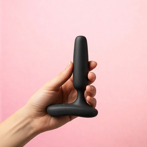 Lovense Glint Touch-Responsive Vibrating Butt Plug Black held in hand against a pink background.