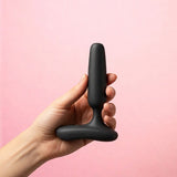 Lovense Glint Touch-Responsive Vibrating Butt Plug Black held in hand against a pink background.