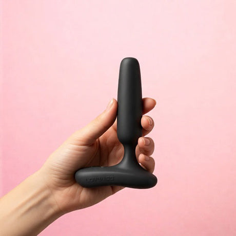 Lovense Glint Touch-Responsive Vibrating Butt Plug Black held in hand against a pink background.