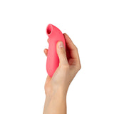 A person holding the Dame Aer Suction Massager Coral, showcasing its ergonomic design and color.