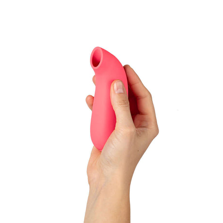 A person holding the Dame Aer Suction Massager Coral, showcasing its ergonomic design and color.