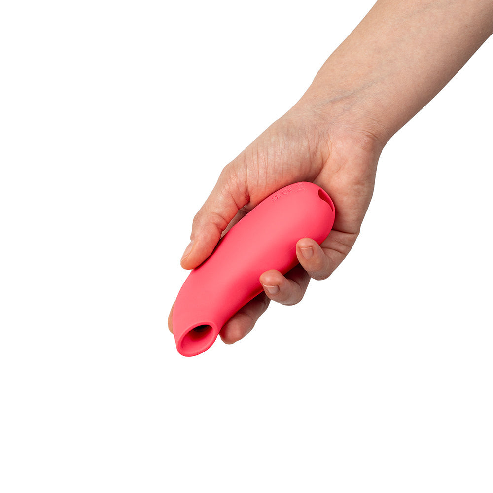 Hand holding the Dame Aer Suction Massager Coral showcasing its sleek design and ergonomic shape.