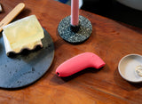 Dame Aer Suction Massager Coral resting on a wooden surface with soap and a candle holder.