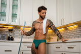 Male Power Ripple Moon Jock Teal S/M worn by a muscular man in a stylish kitchen setting.