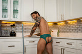 Male Power Ripple Moon Jock Teal S/M worn by a muscular man in a kitchen, showcasing modern lace design.