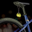 Teeny Weeny Light-Up Silicone Truck Nuts Black hang from a bike seat, glowing yellow to add humor and visibility.