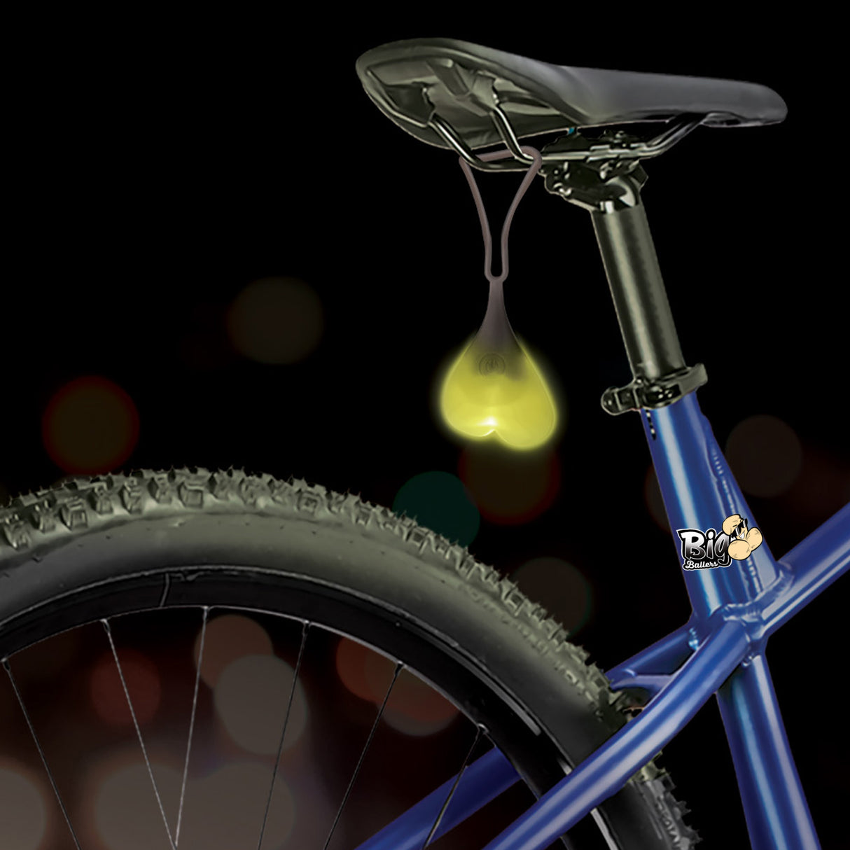 Teeny Weeny Light-Up Silicone Truck Nuts Black hang from a bike seat, glowing yellow to add humor and visibility.