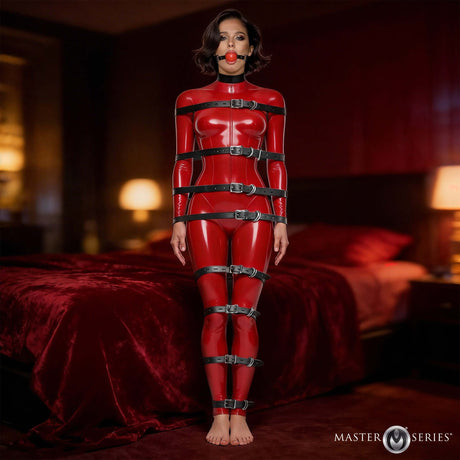 Master Series Backbone Full Body Harness Black worn by a model in a provocative pose on a bed.