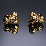 Gold bowknot binder clip style nipple clamps with elegant embossed design, reflecting on a dark surface.