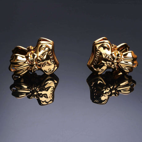 Gold bowknot binder clip style nipple clamps with elegant embossed design, reflecting on a dark surface.