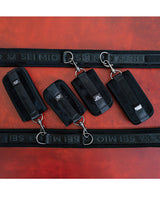 Sei Mio Pretty Thighed Up Thigh Wrist and Ankle Restraint black bondage gear set on a textured red background.