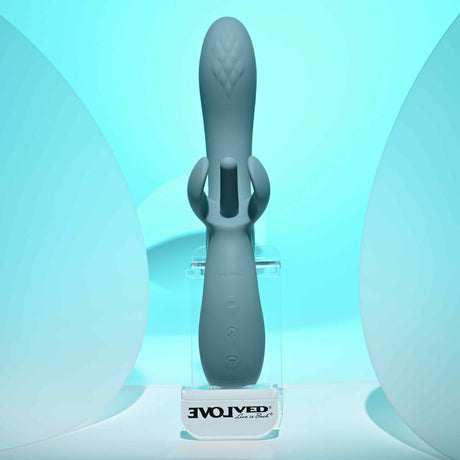 Evolved Take Your Flick Dual Motor Rabbit Vibrator displayed on clear stand against a soft blue background.