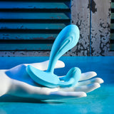 Gender X Wear Me Out Wearable Dual Vibrator Blue held in a white hand against a textured blue background.