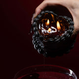 Heart-shaped wax candle with two flames, held above a bowl, showcasing its stylish red-and-black design.