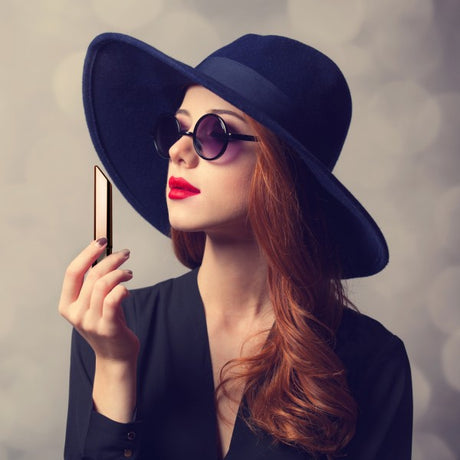 Woman wearing a large navy hat and sunglasses, holding a gold object, exuding elegance and style.