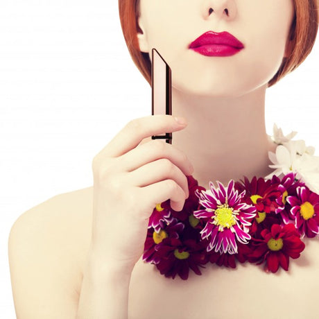 Woman holding a sleek item with red lips and a floral necklace, presenting style and elegance.