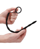 Ouch Urethral Sounding Silicone Plug & Cock Ring Black held in hands, showcasing its design and flexibility.