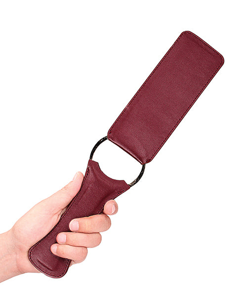 Shots Ouch Halo Paddle Burgundy held by a hand, showcasing its elegant burgundy finish and design.