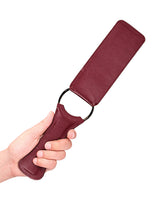 Shots Ouch Halo Paddle Burgundy held by a hand, showcasing its elegant burgundy finish and design.
