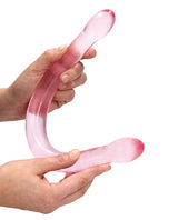 Shots RealRock Crystal Clear 17 Inch Double Dildo Pink held in hands, showcasing its smooth and translucent design.