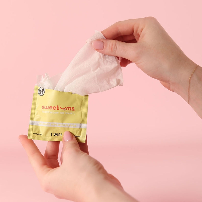 Person holding Sweetums Pina Colada Flavored Intimate Wipes packaging with a wipe partially pulled out.