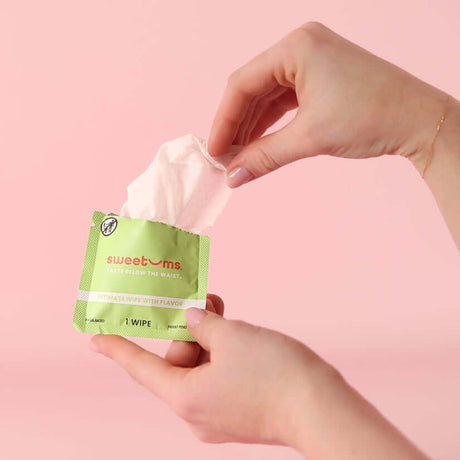 Hand holding Sweetums Watermelon Flavored Intimate Wipes packet with a wipe partially pulled out.