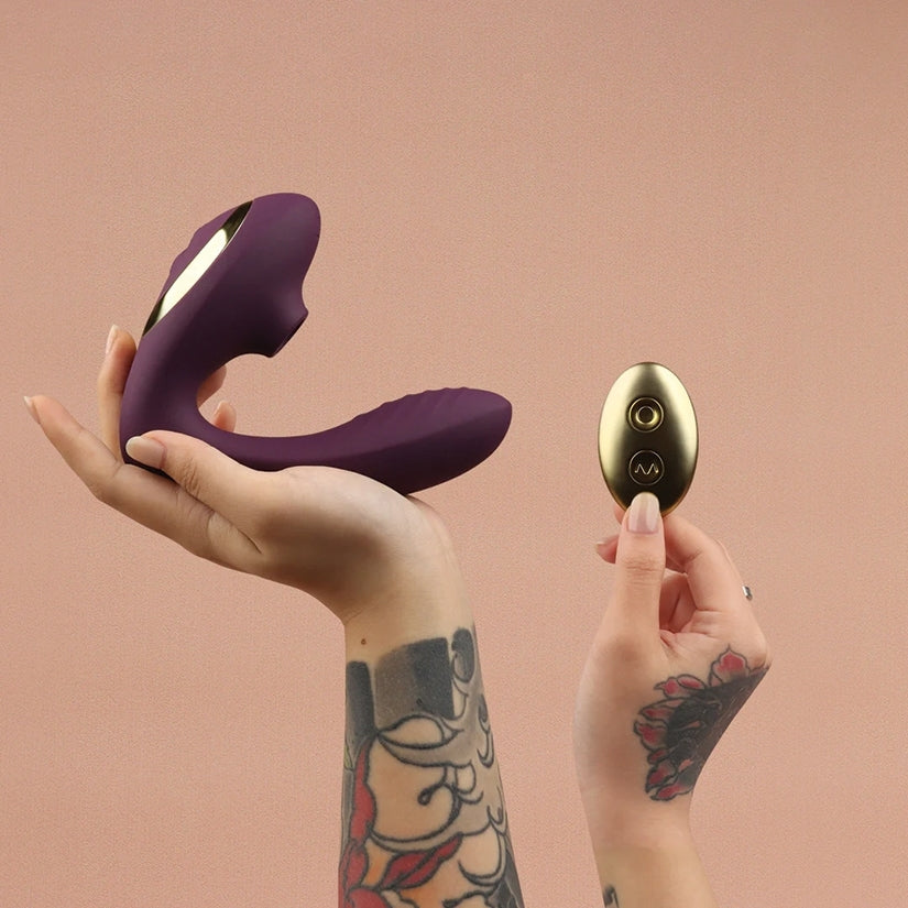 Tracy's Dog OG2 Clitoral Sucking Vibrator Purple with wireless remote in hands against a pink background.