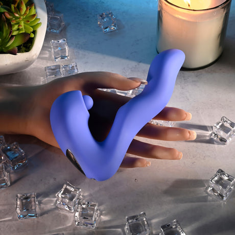 Evolved Tappity Tap Silicone Vibrator Blue held in a hand, surrounded by ice cubes and a candle.