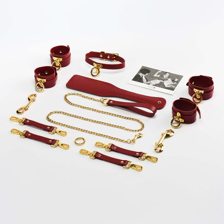 Luxury red Italian leather bondage tools set with gold accents, including cuffs, leash, and accessories in a polished arrangement.