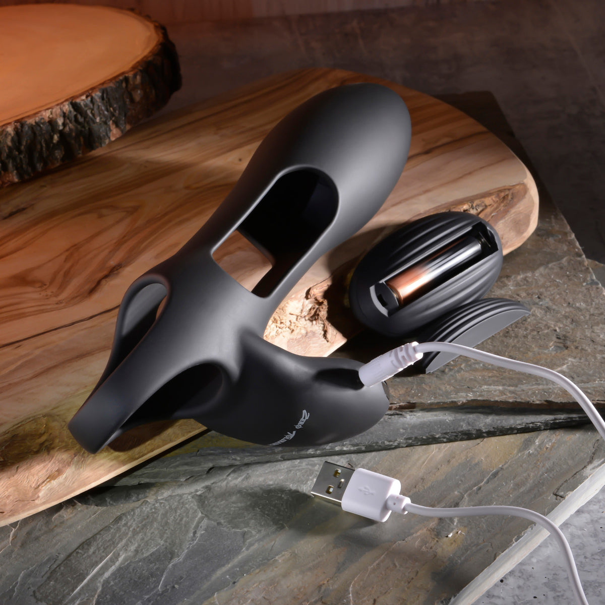 Zero Tolerance Nautilus Vibrating Penis Sleeve Black on a wooden surface with USB charging cable.